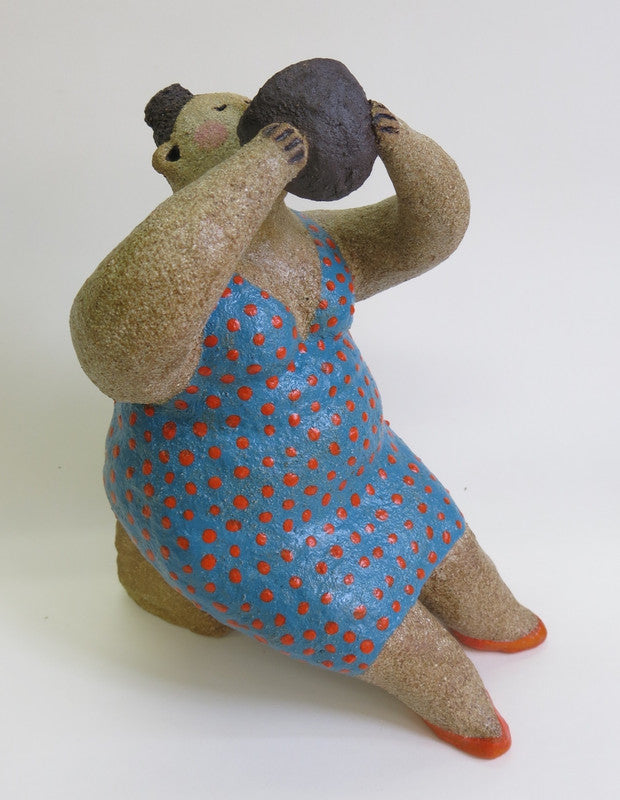 A textured sculpture of a seated figure in a blue dress with red polka dots, holding a dark round object to its mouth.
